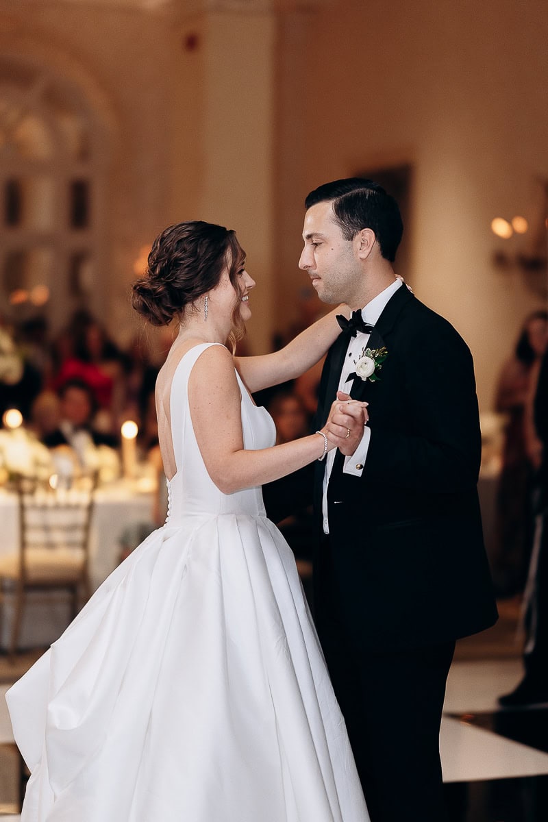 Bride in structured white gown and groom in black tuxedo share a close first dance at an elegant indoor wedding reception at Westchester Country Club, Rye, NY.