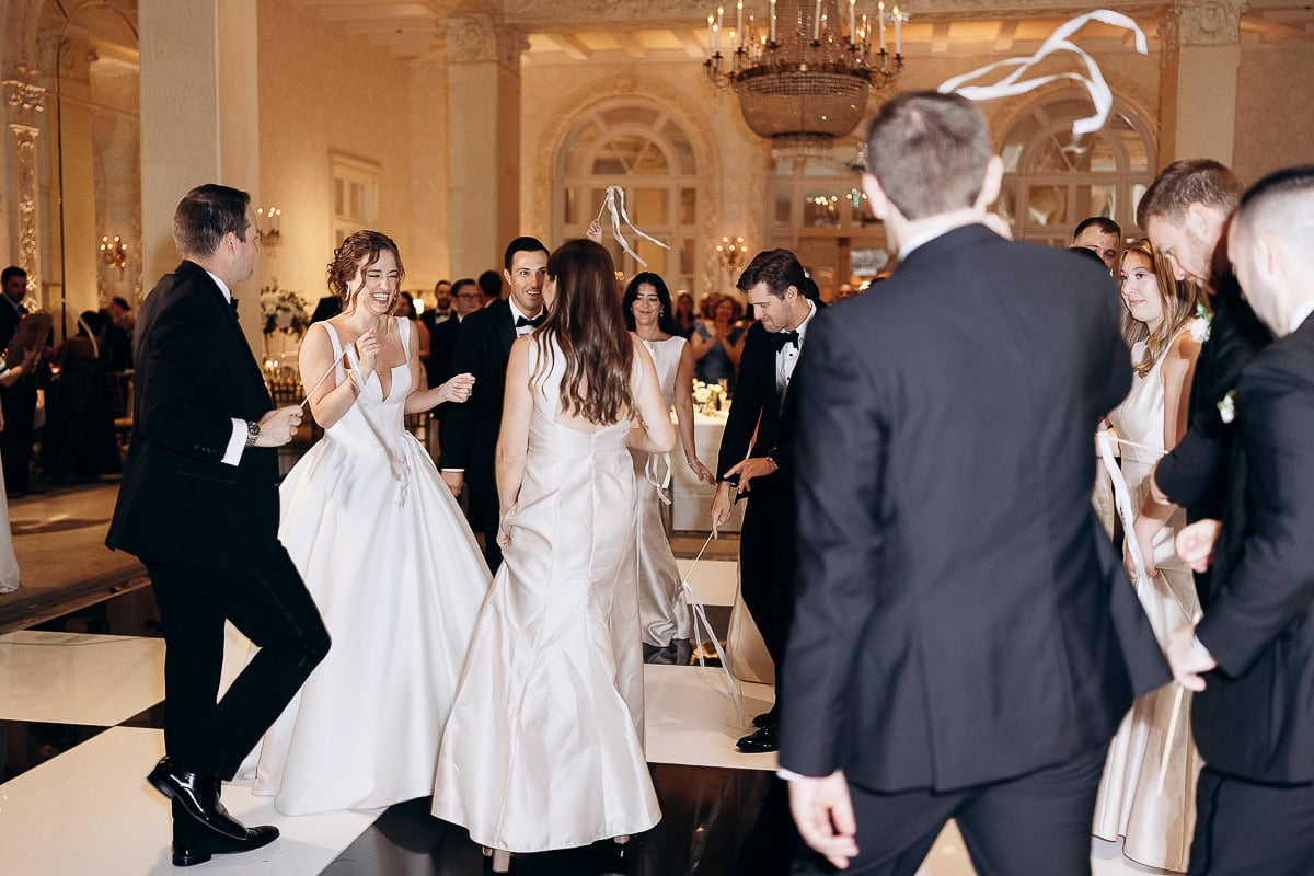 Guests in formal attire dancing with white ribbons on a black-and-white checkered floor under a chandelier at Westchester Country Club, Rye, NY.