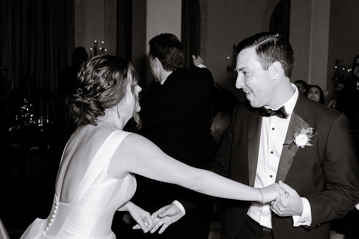 Black and white photo of a bride and groom dancing, the bride in a low-back satin gown and the groom in a tuxedo with boutonniere, at Westchester Country Club.