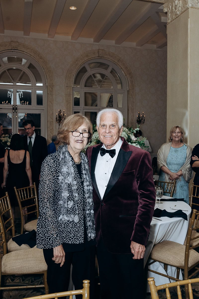 Mature couple dressed in formal attire standing inside a grand room with arched windows and ornate decor at Westchester Country Club, Rye, NY.