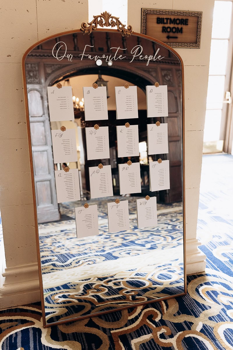Gilded mirror seating chart with escort cards arranged alphabetically, reflecting ornate wood paneling and patterned carpet at Westchester Country Club, Rye NY.