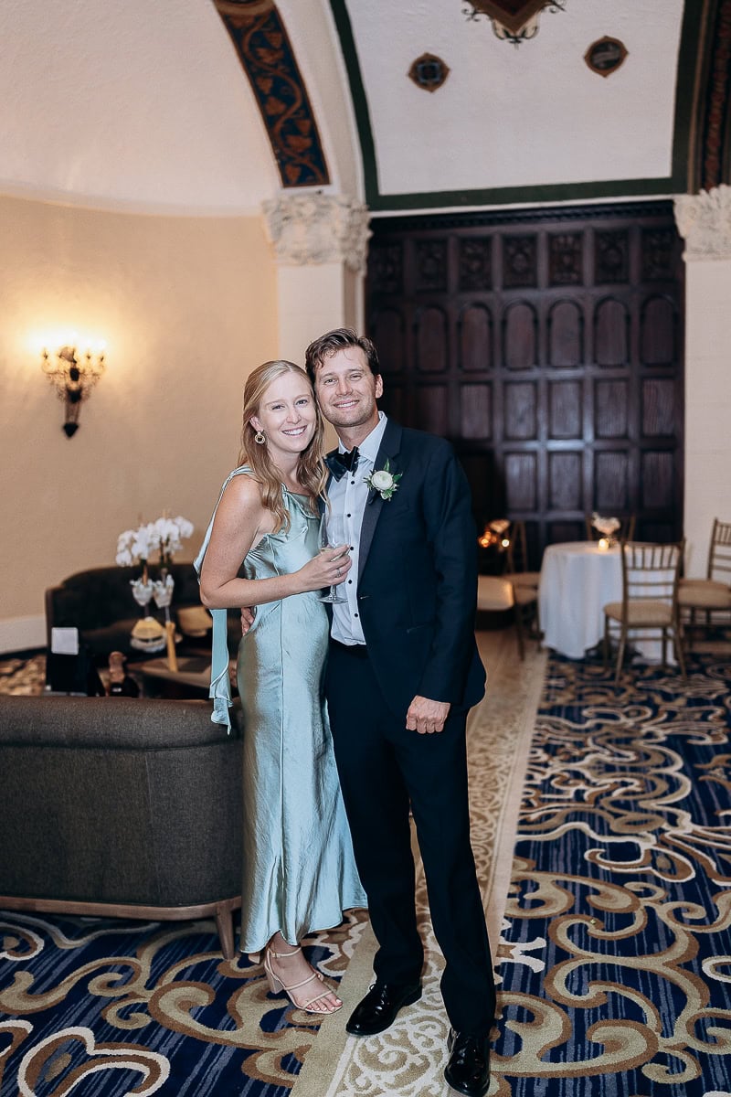 Couple posing in formalwear inside Westchester Country Club with ornate carpet, dark wood paneling, and classic wall sconces.