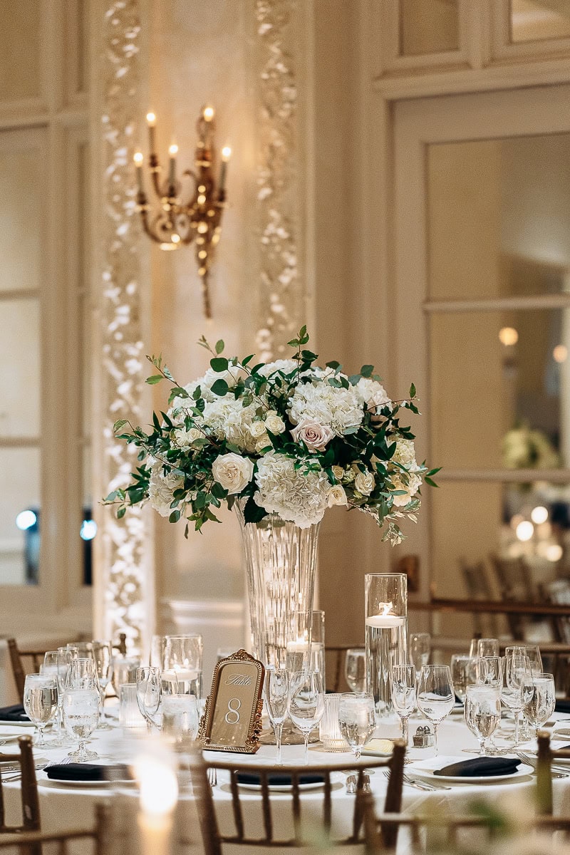 Tall crystal vase with white hydrangeas and roses centerpiece on a round table set with glassware and candles at Westchester Country Club, Rye, NY.