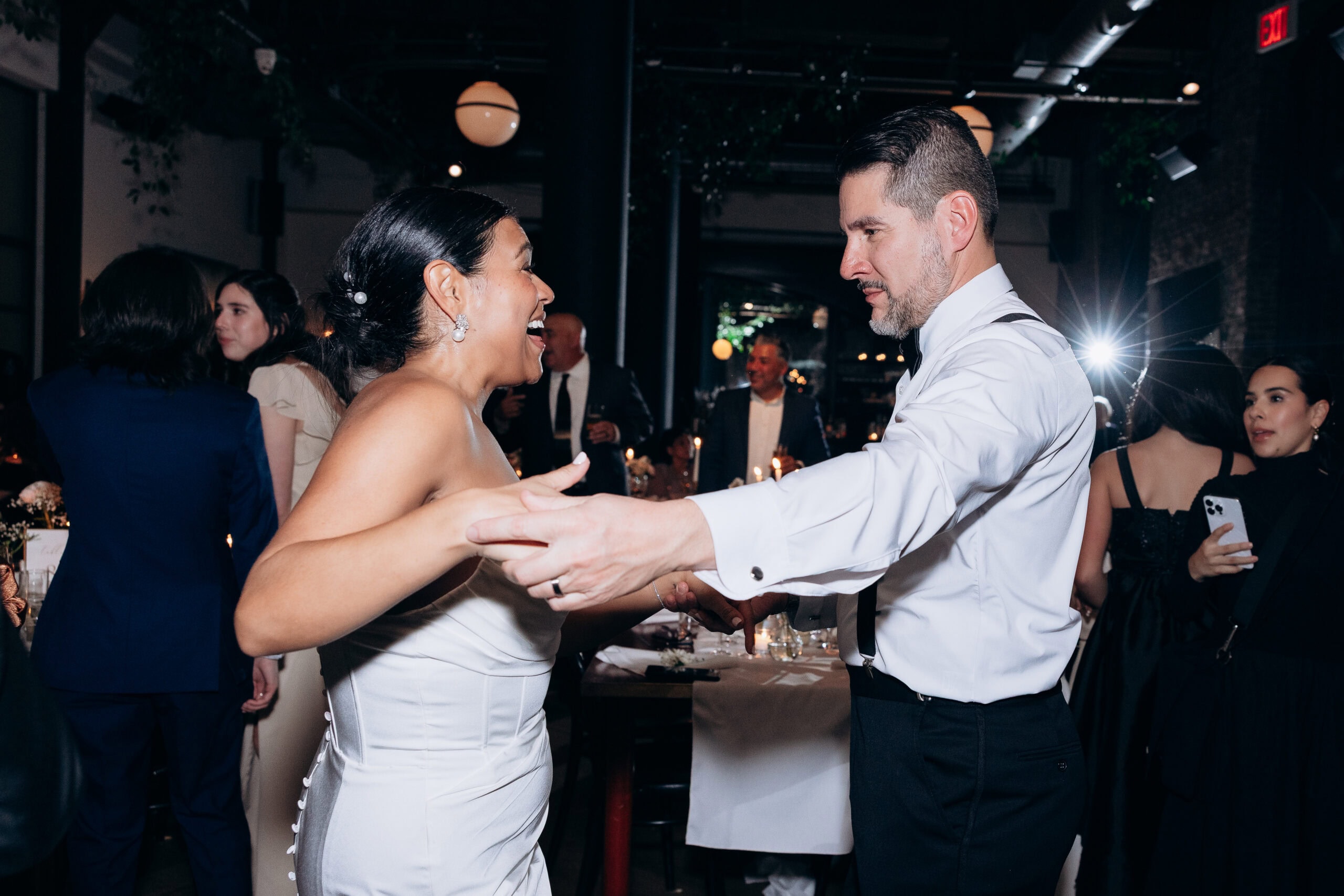 Bride and groom dancing closely at an evening wedding reception with dim lighting and guests in the background at Wythe Hotel, Brooklyn.